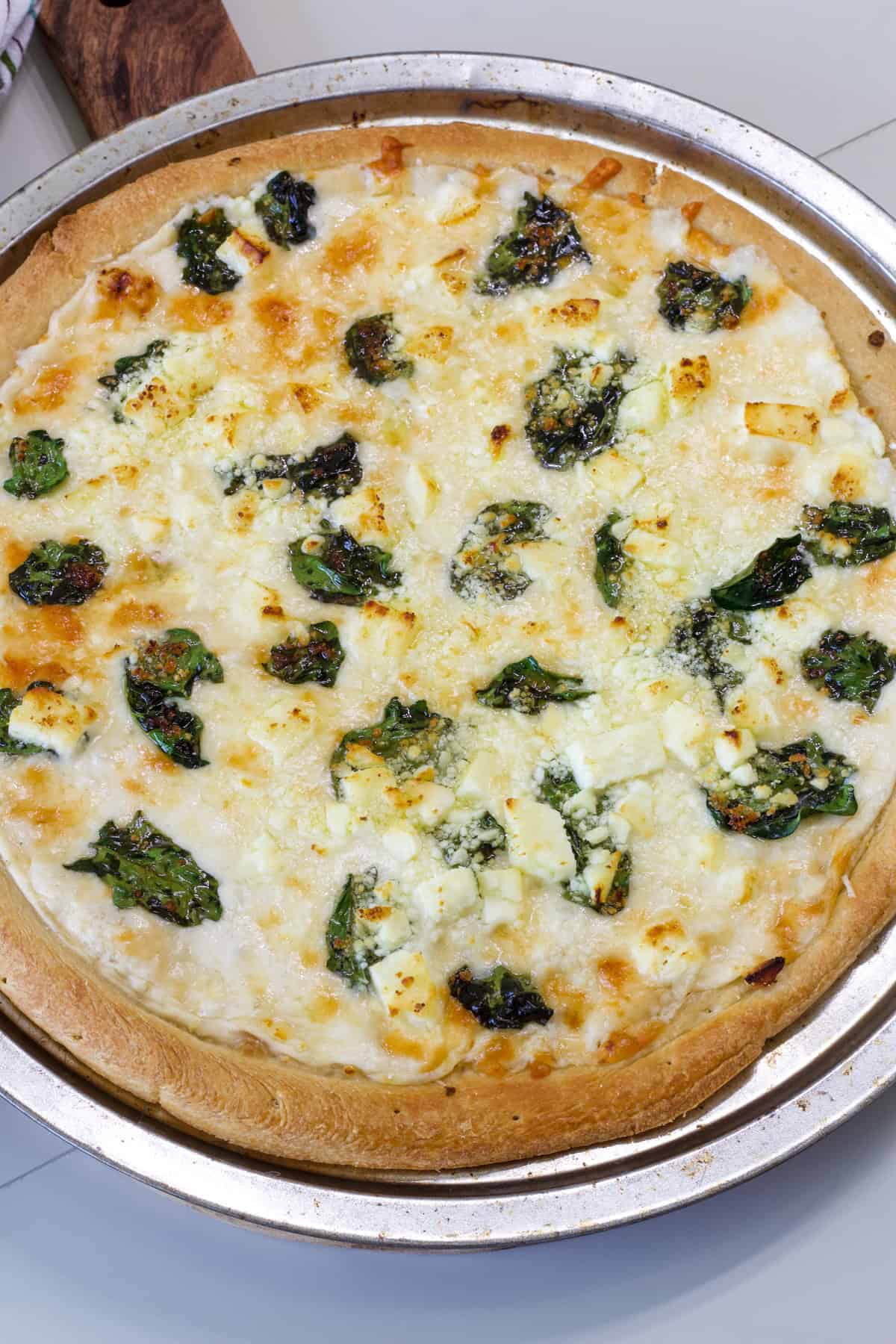 The entire baked Feta Cheese & Spinach White Pizza uncut on a silver pizza pan.