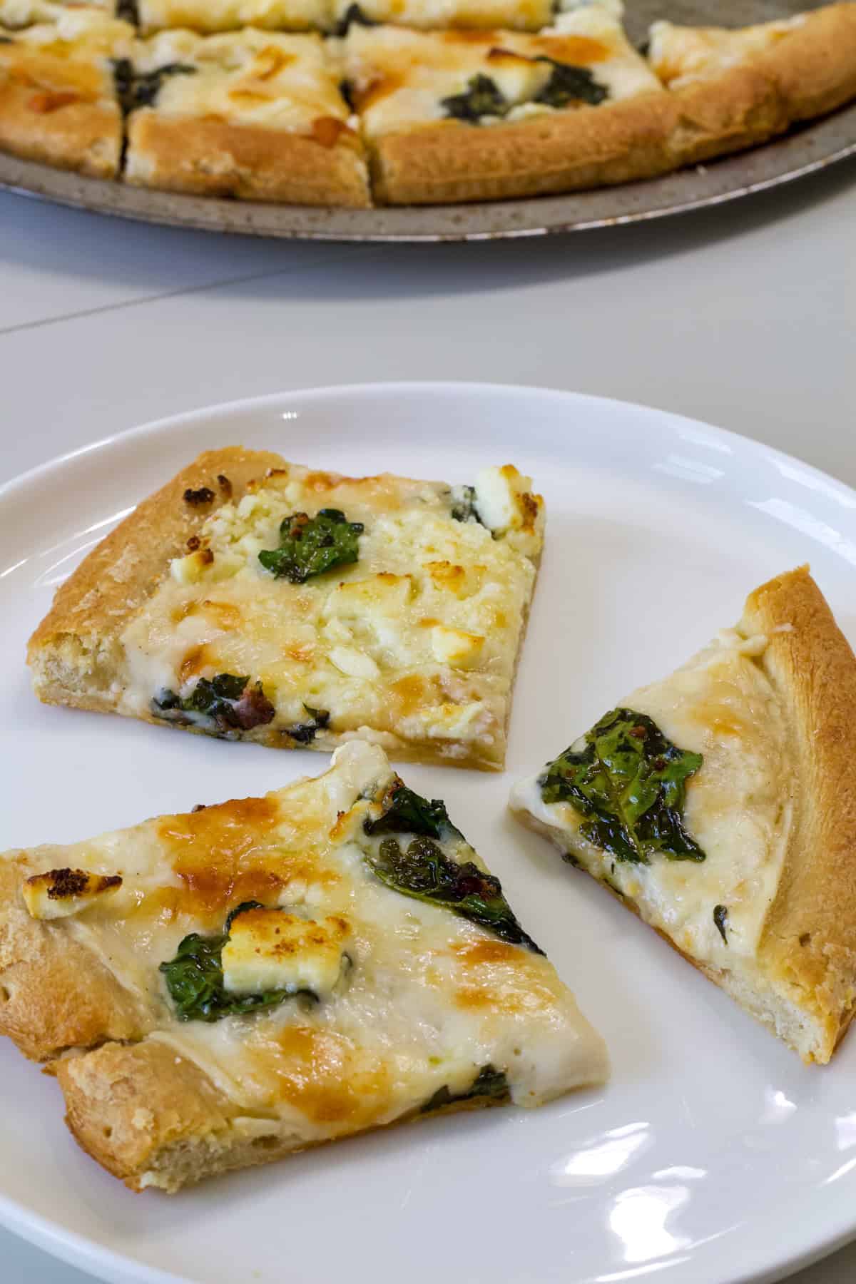 Three pieces of Feta Cheese & Spinach White Pizza on a white plate.