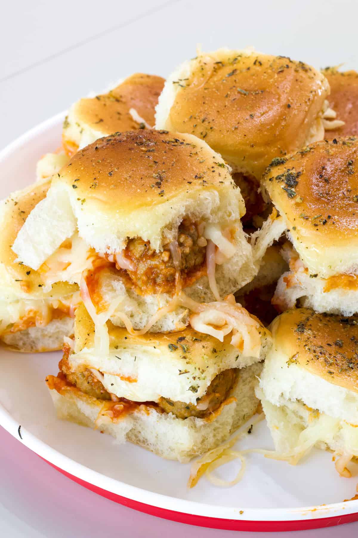 Many Meatball Sliders on Hawaiian Rolls on a white and red serving platter.