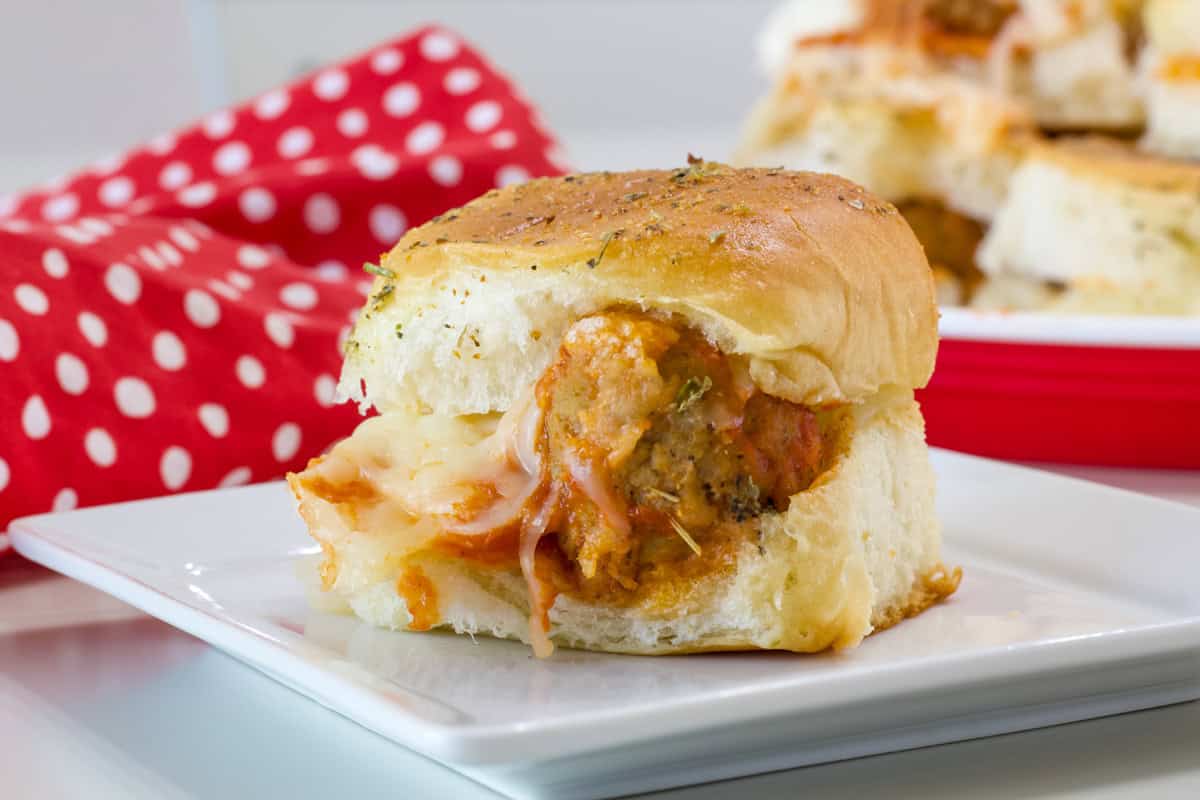 Side view of one Meatball Sliders on Hawaiian Rolls on a small white plate.