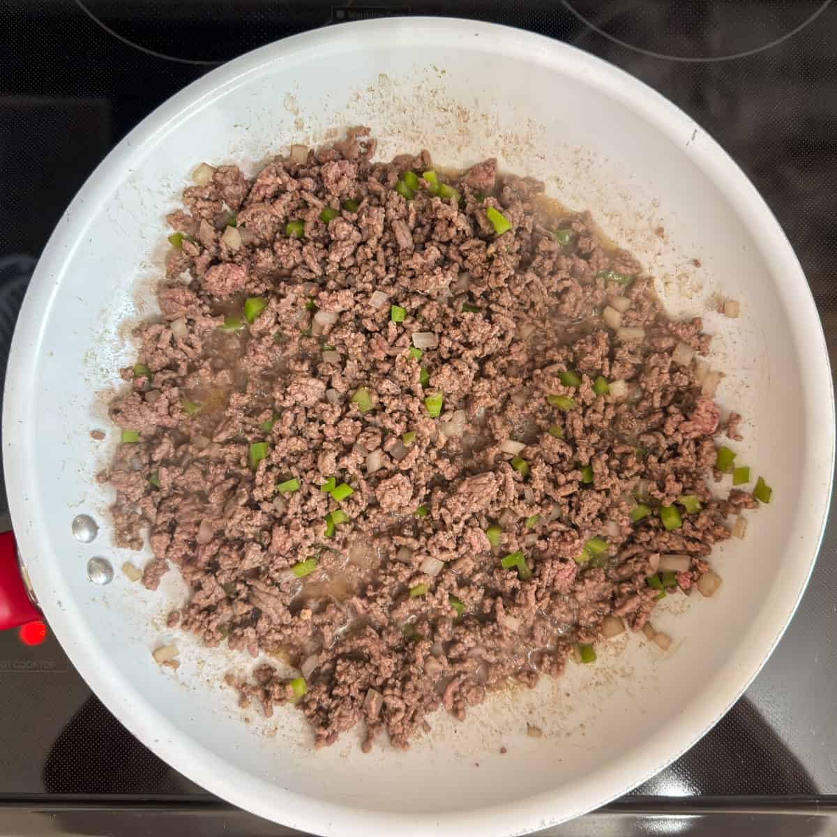 The ground beef, green peppers and onion in the skillet after being browned.