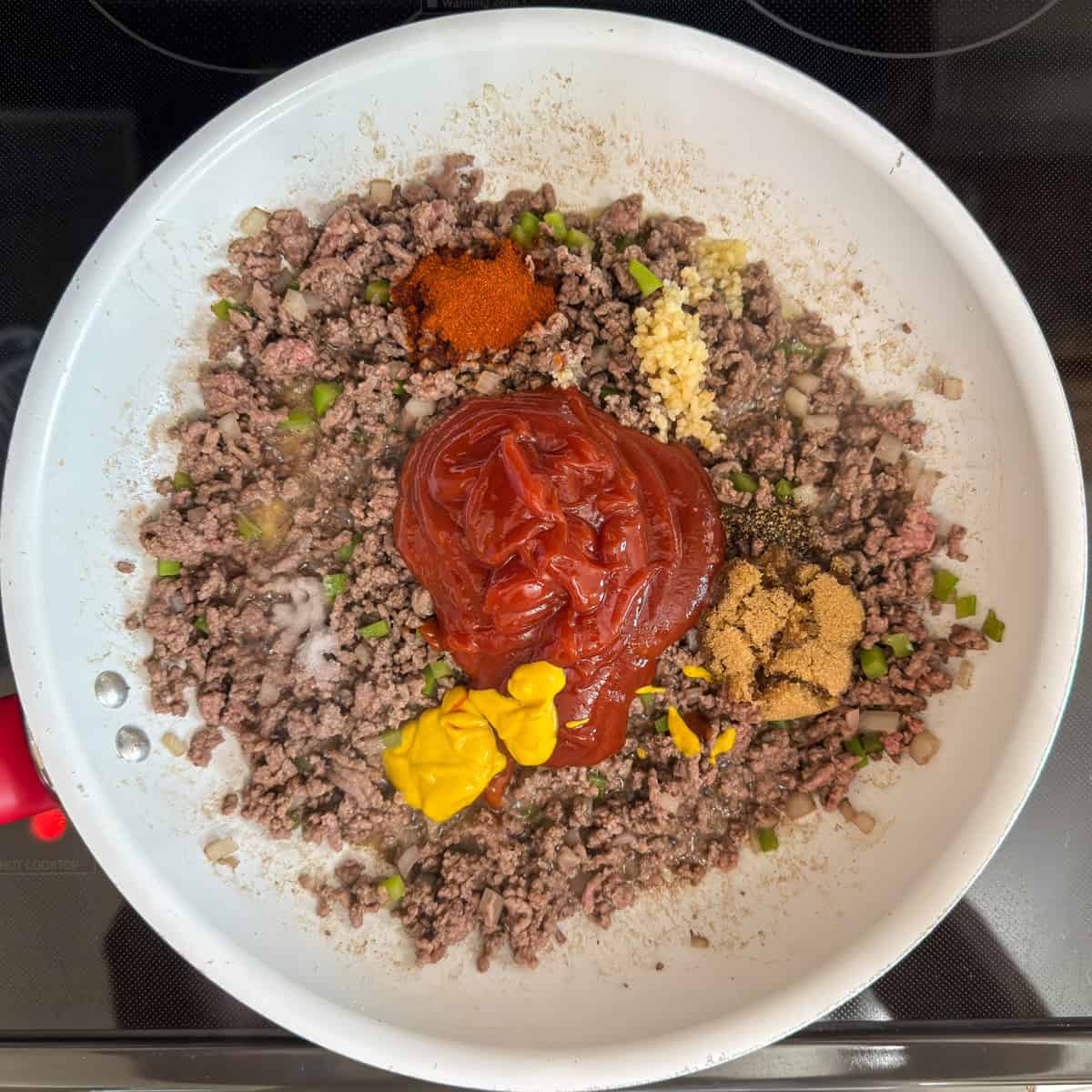 The ketchup, mustard, brown sugar, garlic, paprika, salt and pepper added on top of the beef mixture.