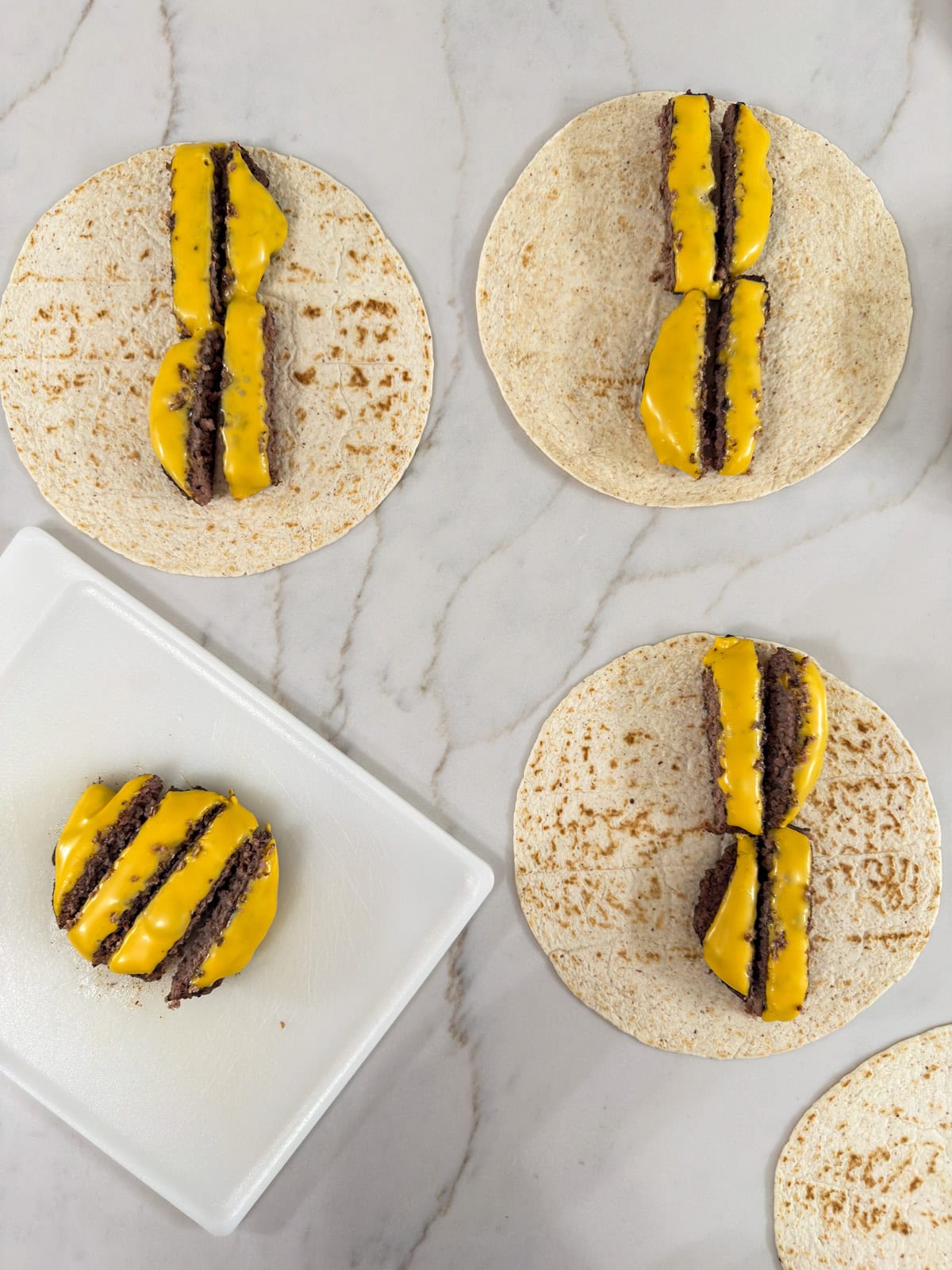 The cut burger patties, one on the cutting board and three on the tortillas.