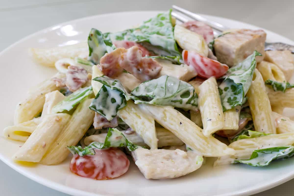 Side close up view of one serving of Chicken BLT Pasta Salad on a white plate.
