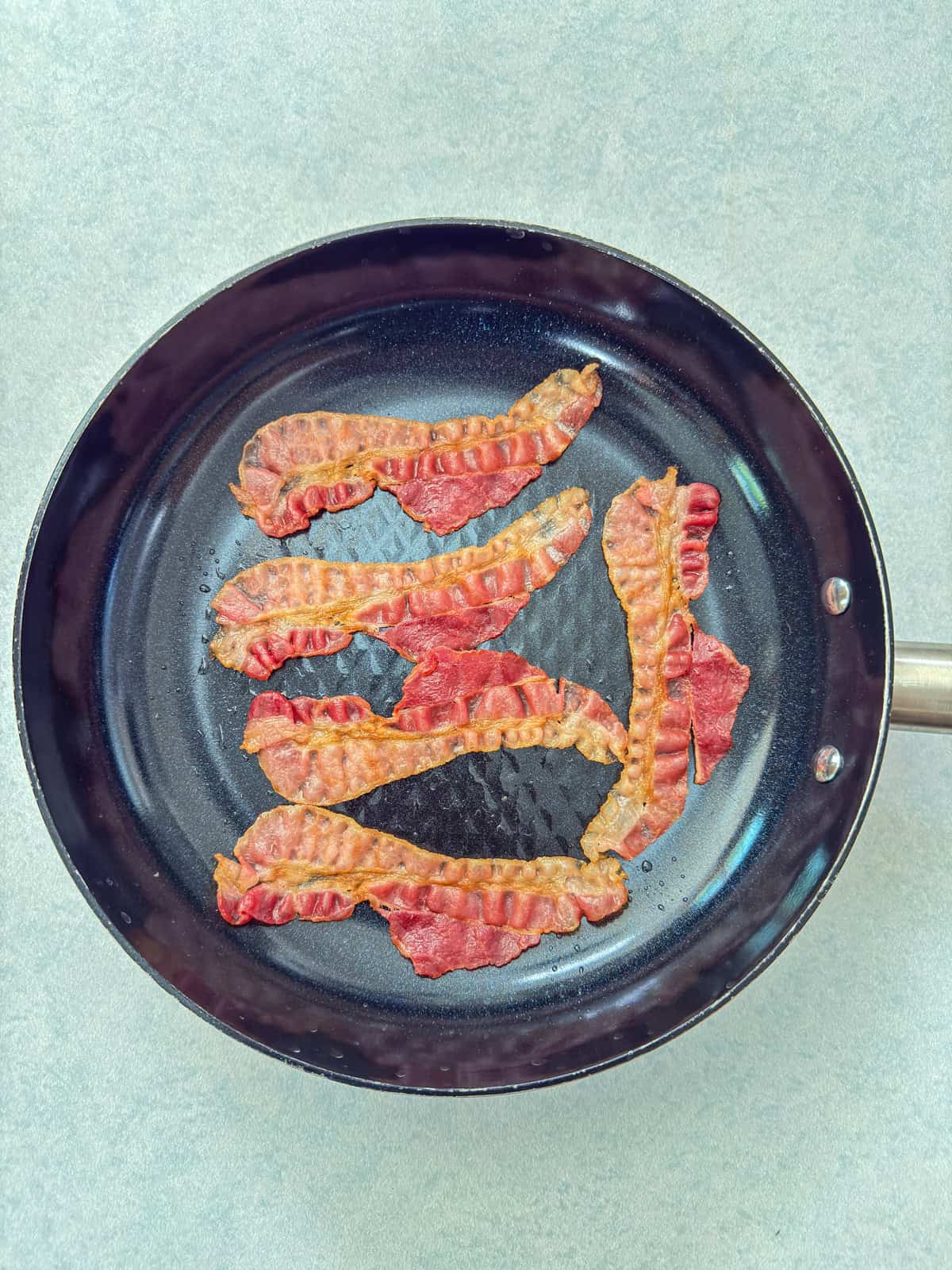 The pre-cooked bacon in a skillet before it's been crisped up.