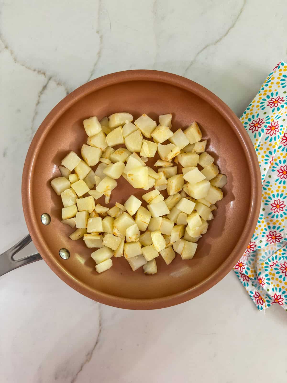 A gold colored skillet with cubed potatoes in it.