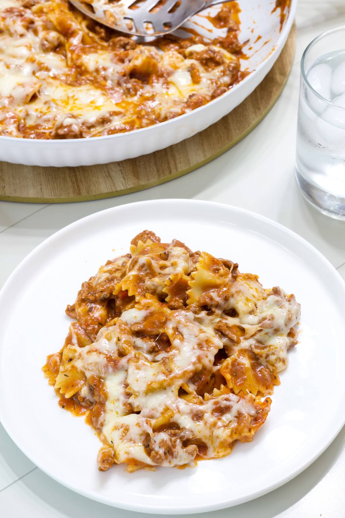 One serving of lasagna in the foreground and the skillet with the remaining in the background.