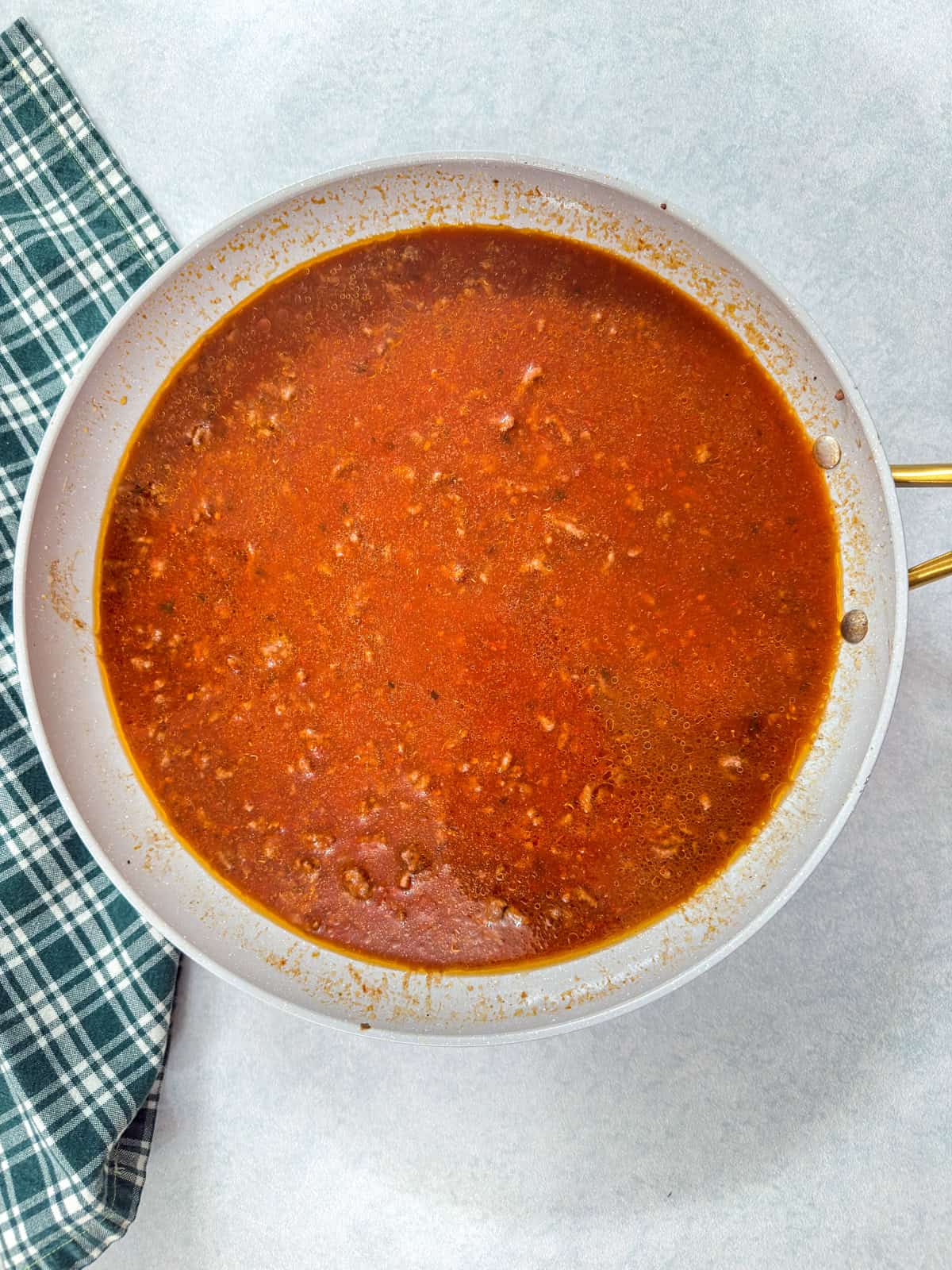 The browned beef, water and pasta sauce in a skillet.