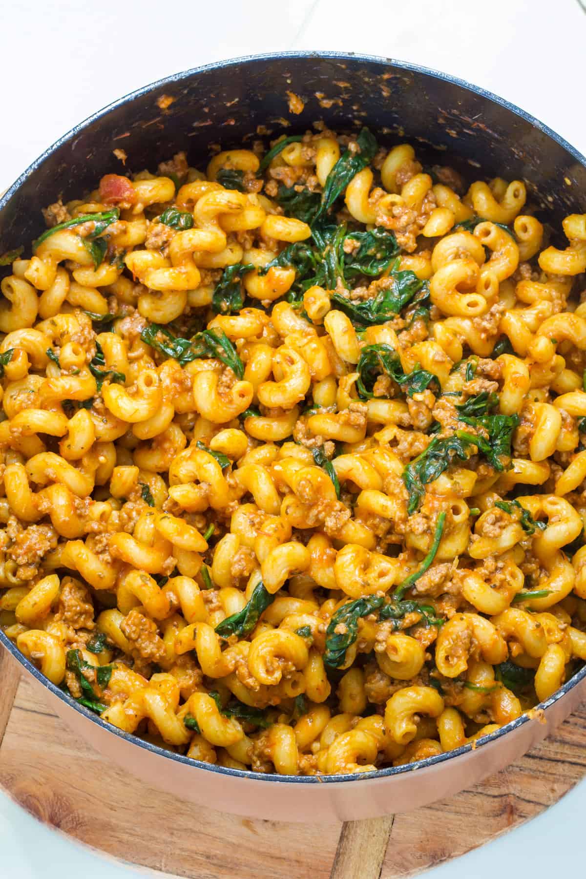 A pan filled with pasta and spinach on a wooden board