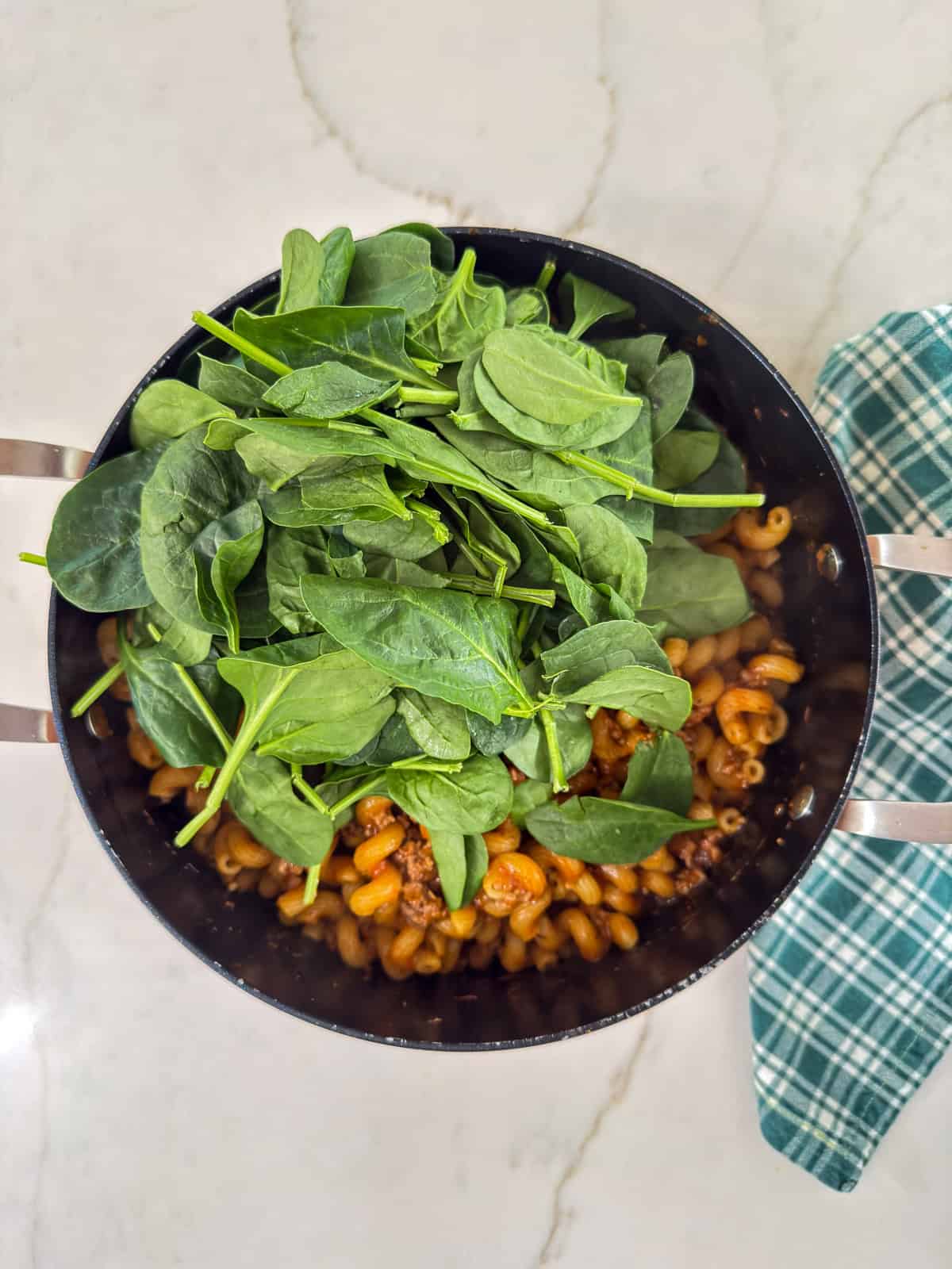 The round beef and pasta with the spinach added, before it's been mixed.