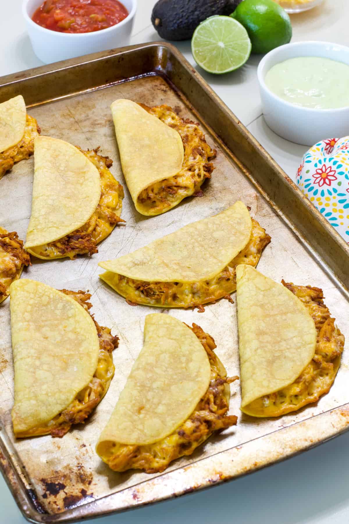 All eight Oven Baked Chicken Tacos on a rimmed baking sheet after they came out of the oven.