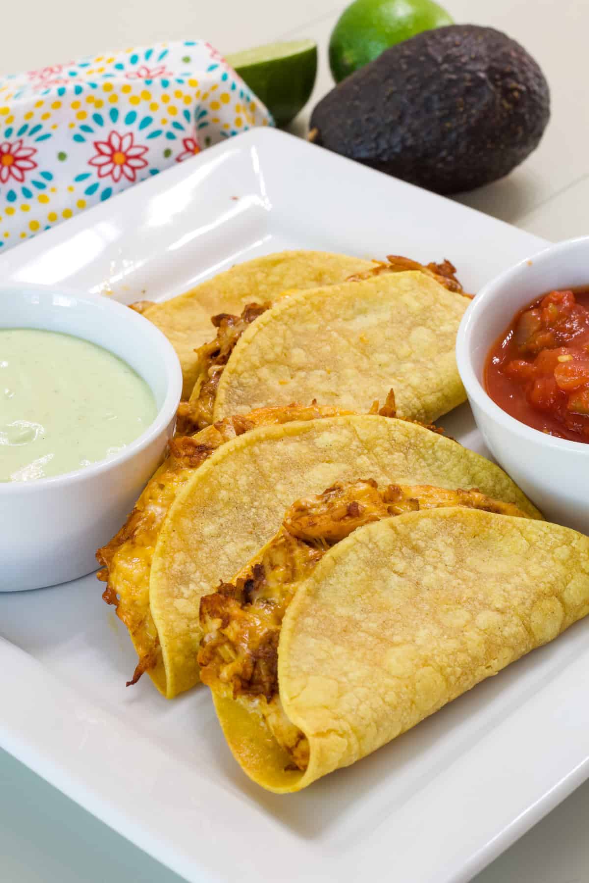 Four Oven Baked Chicken Tacos on a white plate with separate bowls of ranch dipping sauce and salsa.