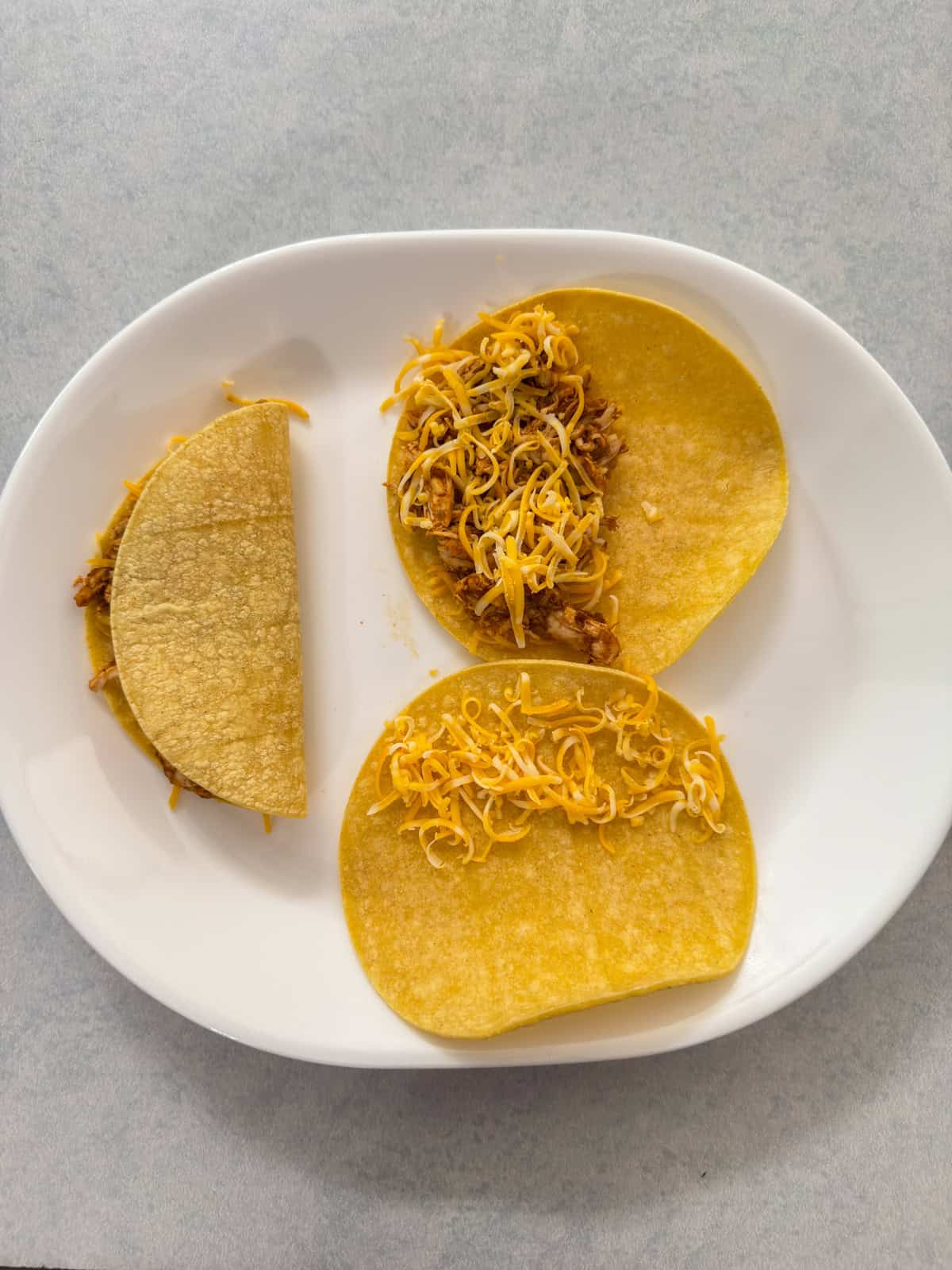 Three tacos, one with just cheese, one with the meat added and one folded over to illustrate how to fill them.