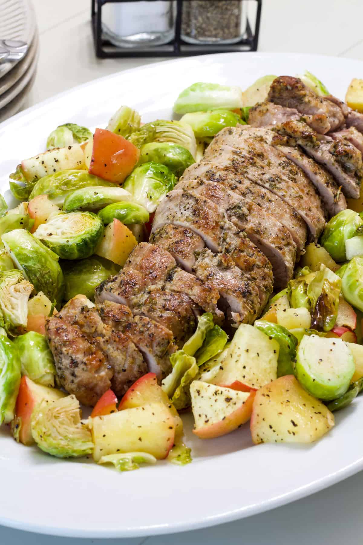 The sliced pork tenderloin on a platter surrounded by the roasted Brussels sprouts and apples.