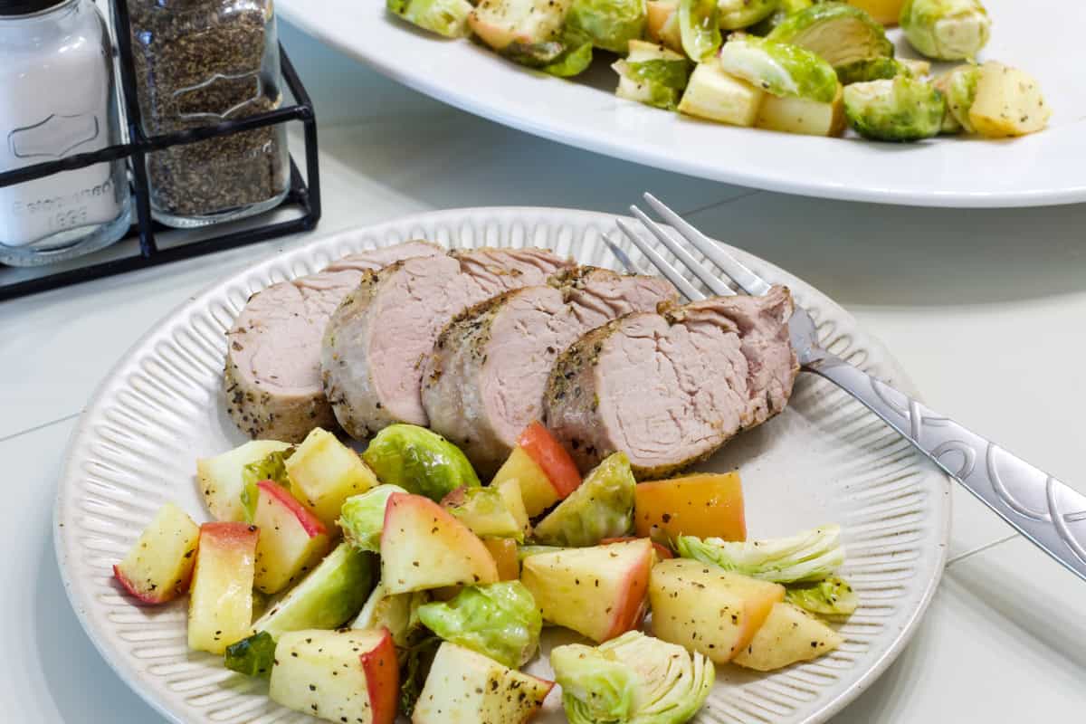 Four pork medallions on a plate with a serving of Brussels sprouts and apples.