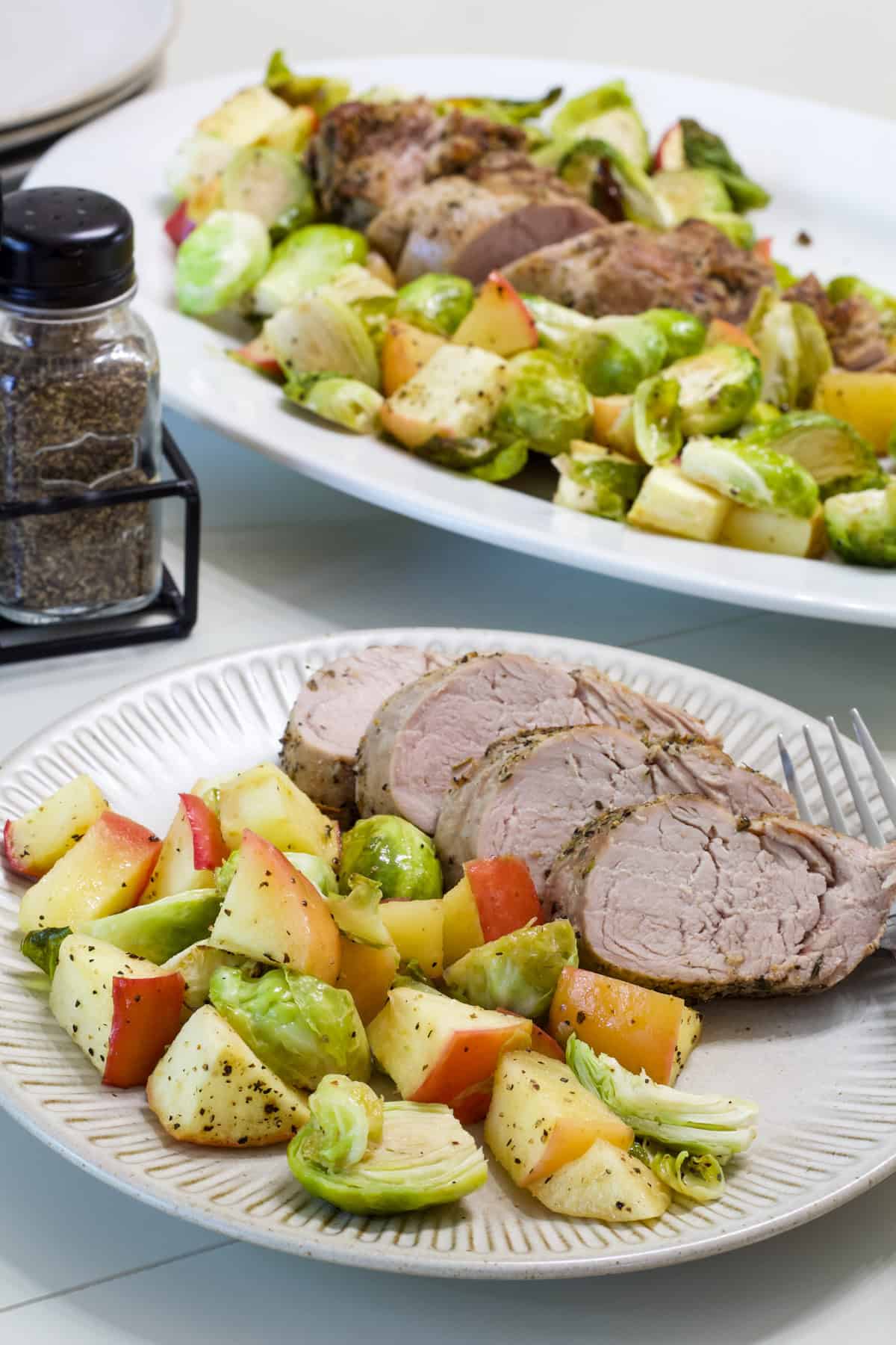 One serving of Pork Tenderloin Brussels Sprouts and Apple Dinner on a plate and the remaining on a platter in the background.