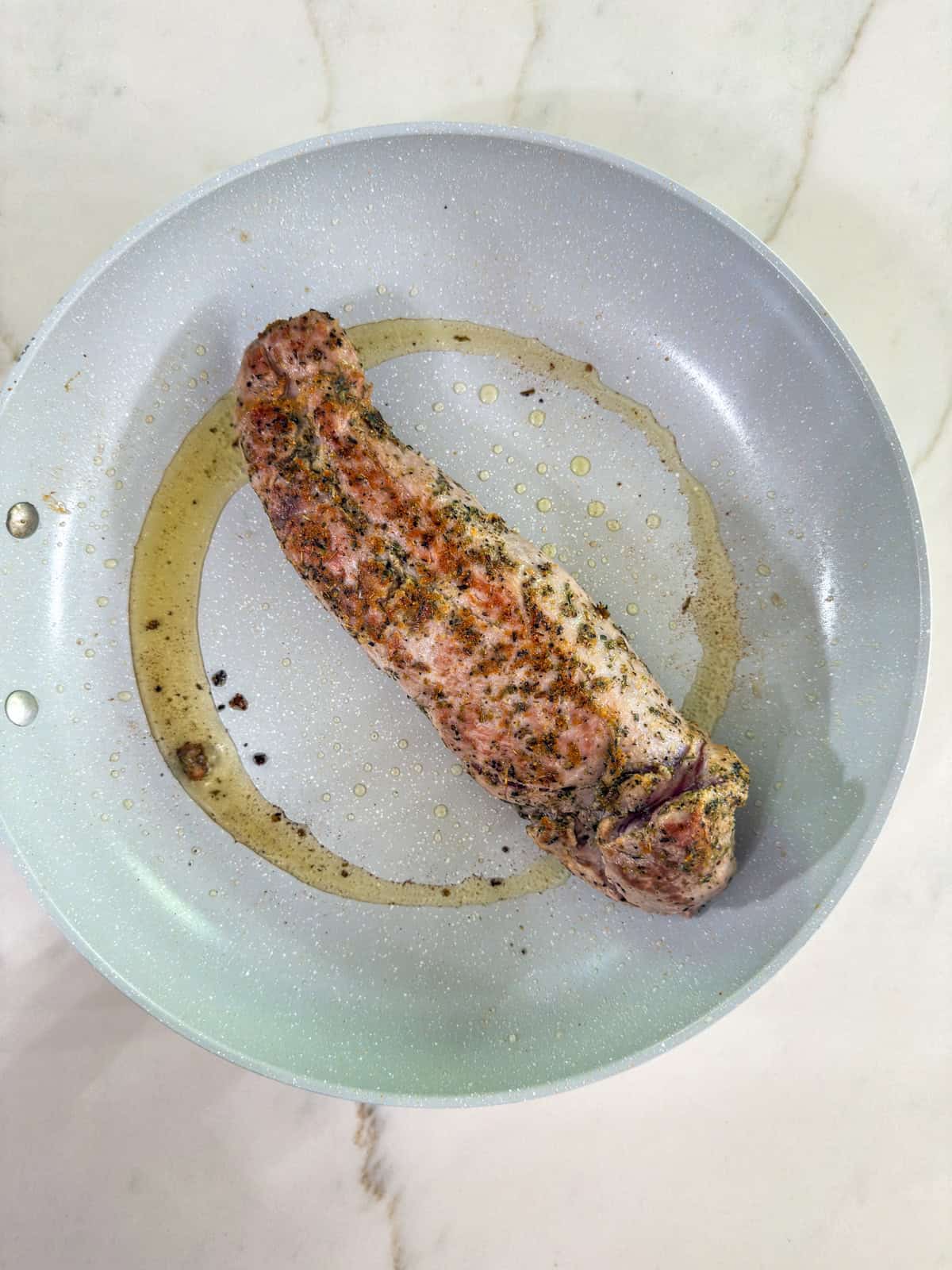 The pork tenderloin in a skillet after it's been seared.