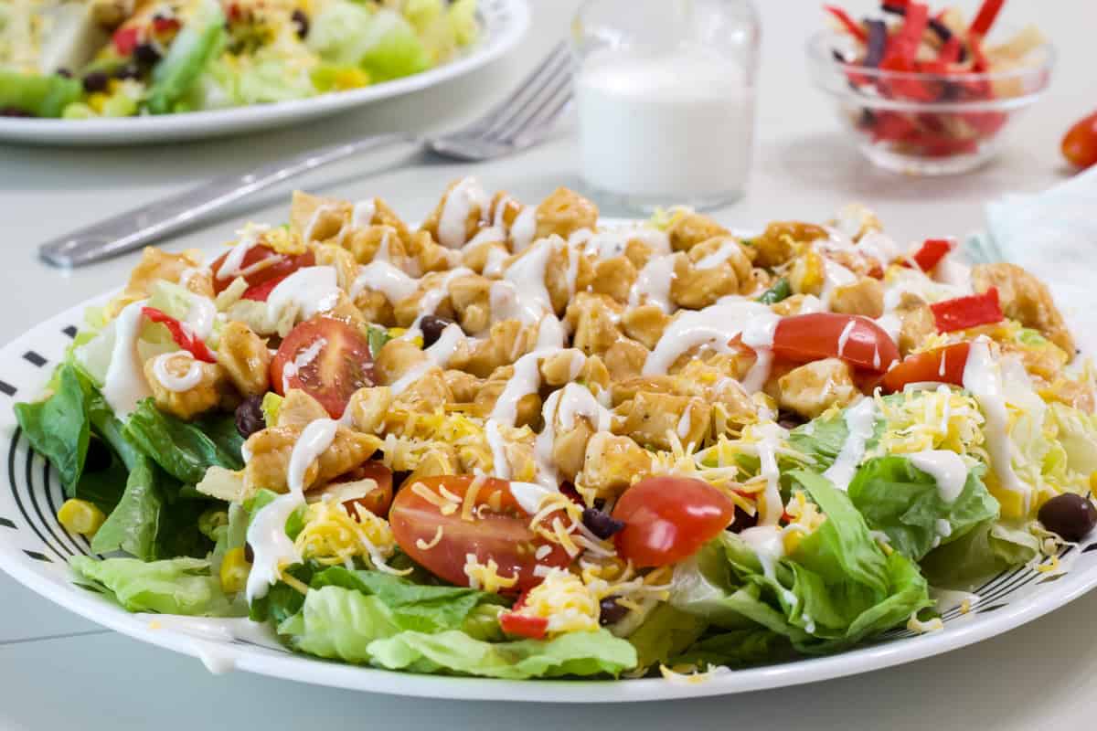 Side view of the Southwest BBQ Chicken Salad on a plate with ranch dressing drizzled over it.