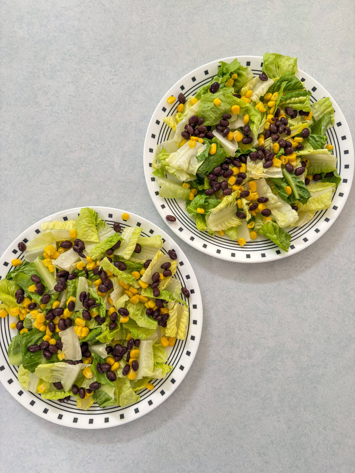 Both salads with a layer of romaine lettuce with corn and black beans on top of it.