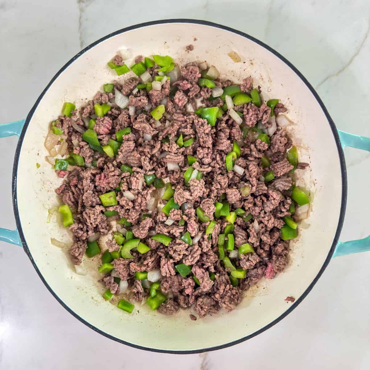 The browned ground beef, onion and green bell pepper in the skillet.